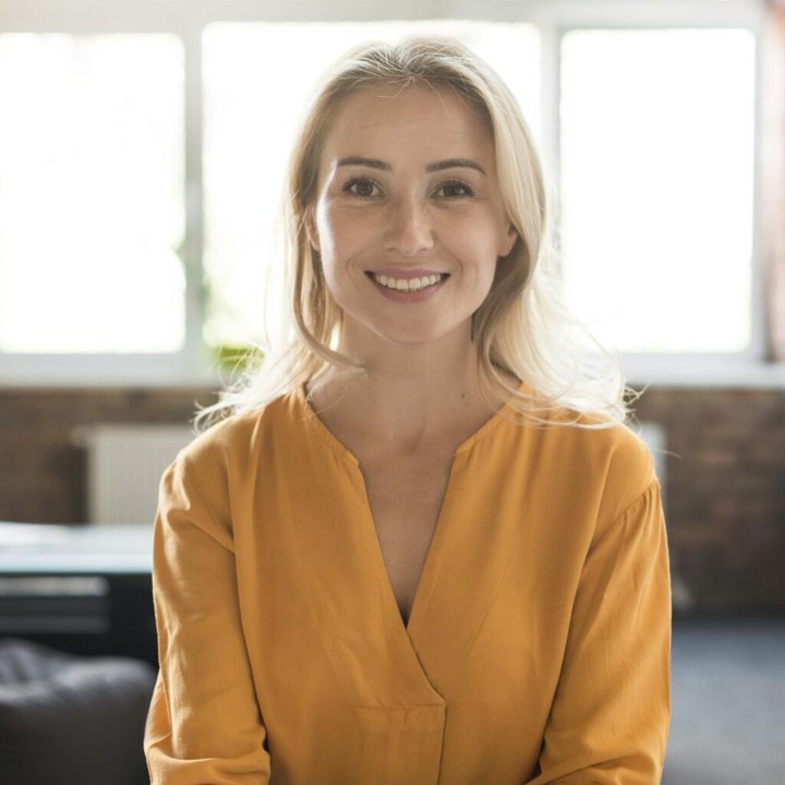 A smiling blonde woman in a mustard blouse in a bright loft