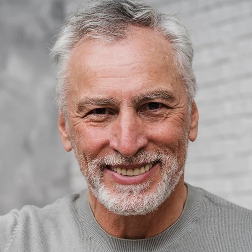 A smiling grey-haired man with a white beard in a grey sweater